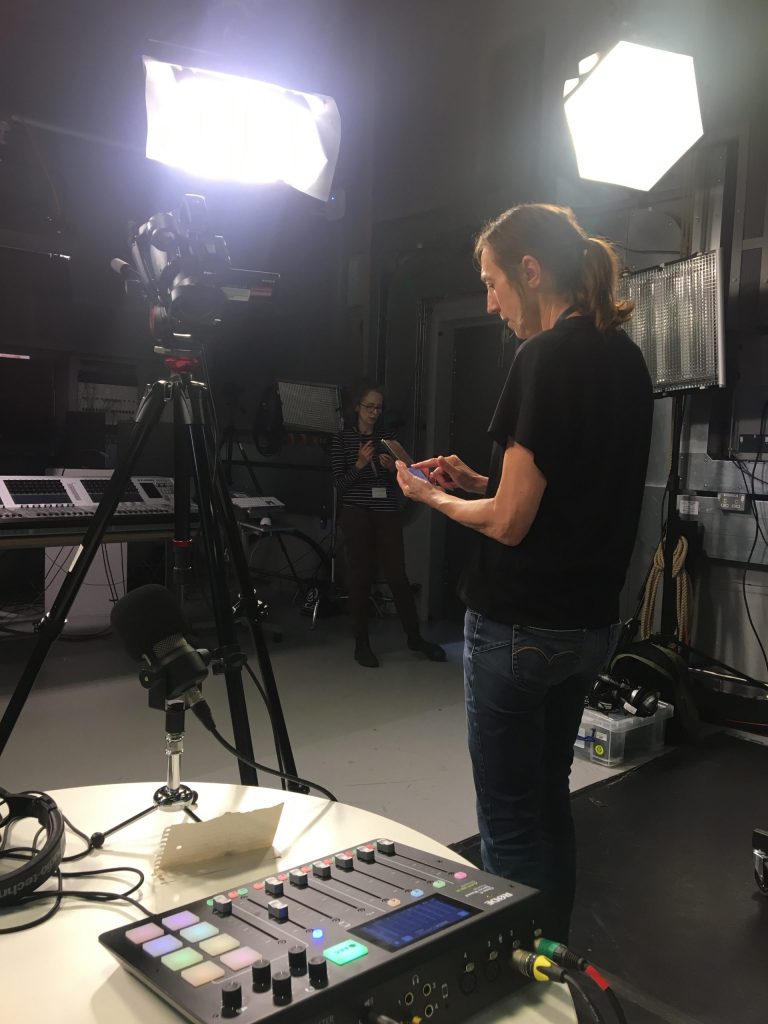A woman on her phone standing in front of a camera in a studio.